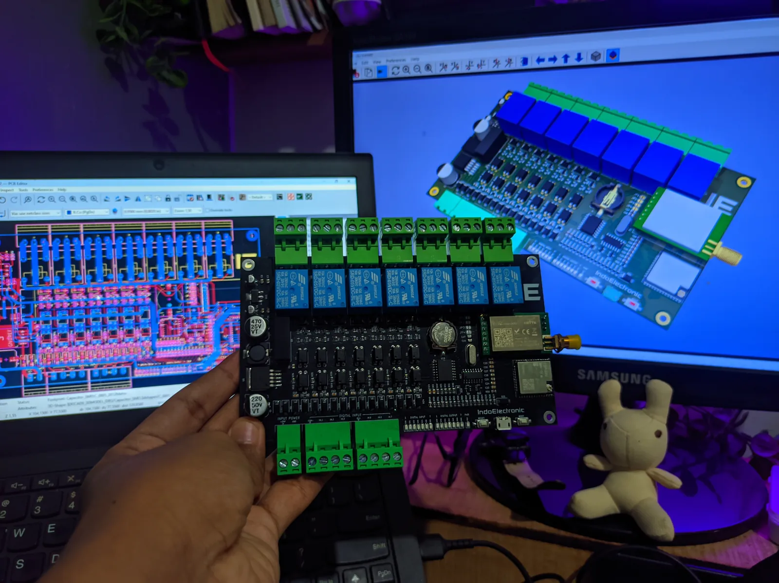 Board PCB hasil produksi dipegang di depan layar desain KiCad